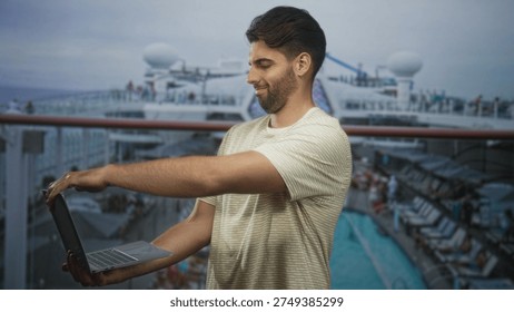 Hispanic man with beard typing on laptop, fingers on keyboard, standing on cruise ship deck by pool; remote work focused.