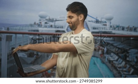 Hispanic man with beard typing on laptop, fingers on keyboard, standing on cruise ship deck by pool; remote work focused.