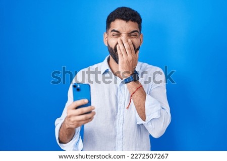 Hispanic man with beard using smartphone typing message laughing and embarrassed giggle covering mouth with hands, gossip and scandal concept  Foto d'archivio © 