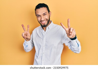 Hispanic man with beard wearing business shirt smiling looking to the camera showing fingers doing victory sign. number two. 
