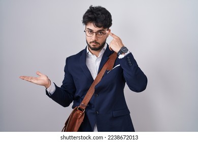 Hispanic man with beard wearing business clothes confused and annoyed with open palm showing copy space and pointing finger to forehead. think about it.  - Shutterstock ID 2238672013
