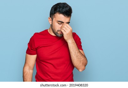 Hispanic Man With Beard Wearing Casual Red T Shirt Tired Rubbing Nose And Eyes Feeling Fatigue And Headache. Stress And Frustration Concept. 