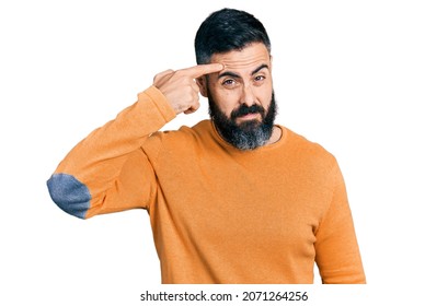 Hispanic Man With Beard Wearing Casual Winter Sweater Pointing Unhappy To Pimple On Forehead, Ugly Infection Of Blackhead. Acne And Skin Problem 