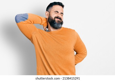 Hispanic man with beard wearing casual winter sweater suffering of neck ache injury, touching neck with hand, muscular pain  - Shutterstock ID 2138415291