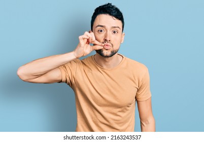 Hispanic man with beard wearing casual t shirt mouth and lips shut as zip with fingers. secret and silent, taboo talking 