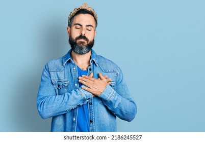 Hispanic Man With Beard Wearing King Crown Smiling With Hands On Chest With Closed Eyes And Grateful Gesture On Face. Health Concept. 