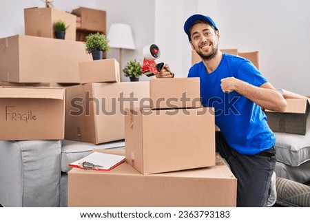 Hispanic man with beard working moving boxes pointing finger to one self smiling happy and proud 
