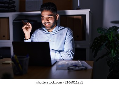 Hispanic Man With Beard Working At The Office With Laptop At Night Smiling Happy Pointing With Hand And Finger To The Side 