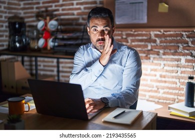 Hispanic Man With Beard Working At The Office At Night Hand On Mouth Telling Secret Rumor, Whispering Malicious Talk Conversation 