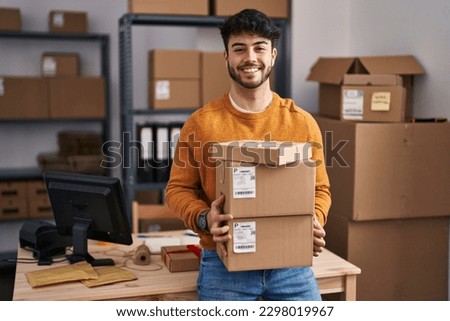 Hispanic man with beard working at small business ecommerce holding packages smiling with a happy and cool smile on face. showing teeth. 