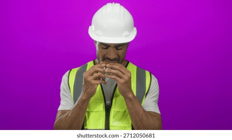 Hispanic man bites waffle while holding wrapper in purple studio; hunger break nourishment satisfaction.