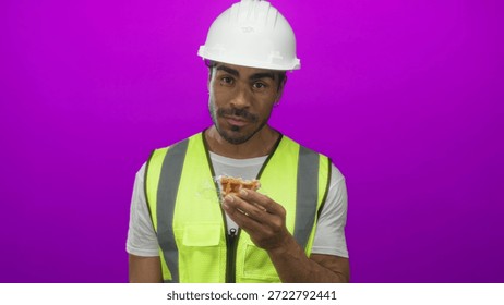 Hispanic man bites waffle while holding wrapper in purple studio; hunger break nourishment satisfaction.
