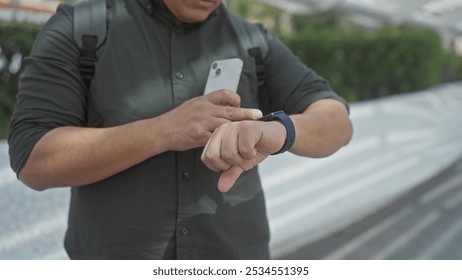 Hispanic man checks smartwatch with smartphone in hand outdoors in the city. - Powered by Shutterstock