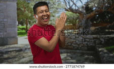 Hispanic man clapping hands in a forest park wearing red shirt and smiling broadly; joy celebration.