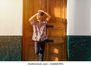 Hispanic Man Combing His Frizzy Hair Leaning Against A Wooden Door At Sunset