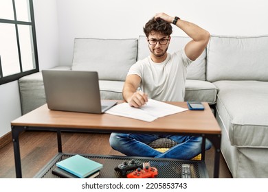 Hispanic Man Doing Papers At Home Confuse And Wondering About Question. Uncertain With Doubt, Thinking With Hand On Head. Pensive Concept. 