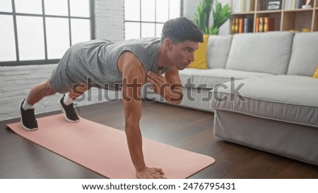 Hispanic man doing push-ups on a mat in a modern living room, showcasing fitness and a healthy lifestyle at home.