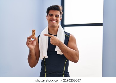 Hispanic Man Eating Protein Bar As Healthy Energy Snack Smiling Happy Pointing With Hand And Finger 