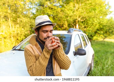 Hispanic man enjoying a cup of coffee leaning on his off-road suv car in the middle of nature. weekend getaway. adventure and leisure time concept.