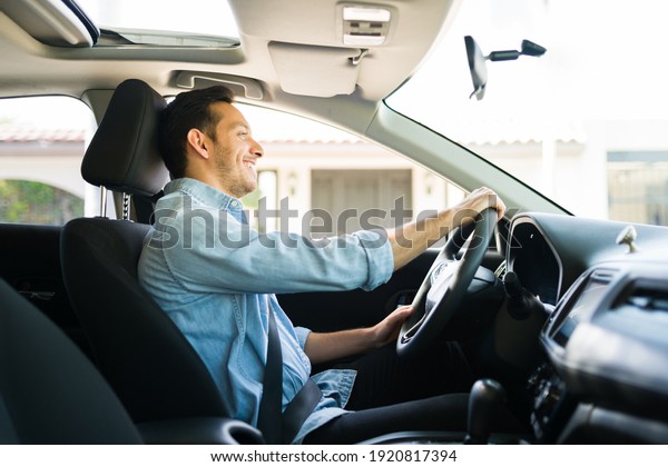 Hispanic man feeling happy while working as a taxi\
driver on a car sharing service of a mobile app. Happy guy driving\
a car during the day