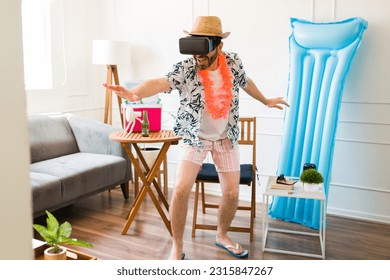 Hispanic man having fun playing with virtual reality glasses pretending to surf on the beach while having summer staycations