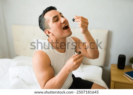 Hispanic man in his bedroom, using a dropper to take his daily cbd oil dose, advocating for a healthy lifestyle and natural remedies