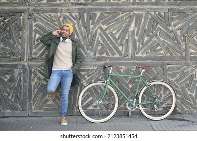 Hispanic Man With His Bicycle Talking On Phone Against Urban Wall.