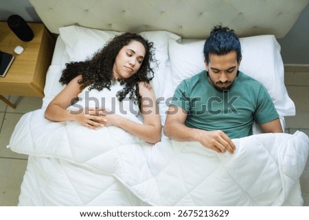 Hispanic man lying in bed, grappling with erectile dysfunction, while his concerned wife sits beside him, sharing the weight of their worries