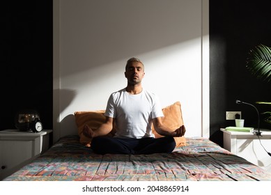 Hispanic man meditating in bedroom illuminated by sunlight. Healthy morning routine concept - Powered by Shutterstock