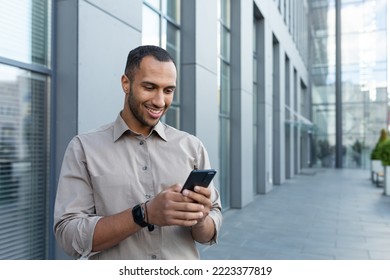 Hispanic Man Outside Modern Office Building Using Smartphone, Businessman In Shirt Typing Message And Browsing Online Pages.