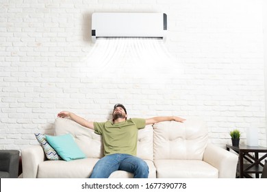 Hispanic Man Relaxing Under Mini Split On Sofa In Living Room At Home