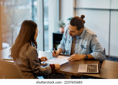 Hispanic man signing a contract while having meeting with financial advisor in the office.