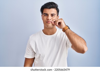 Hispanic Man Standing Over Blue Background Mouth And Lips Shut As Zip With Fingers. Secret And Silent, Taboo Talking 