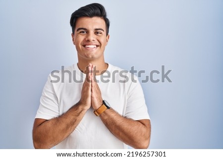 Hispanic man standing over blue background praying with hands together asking for forgiveness smiling confident.  Foto stock © 