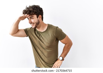 Hispanic man standing over isolated white background very happy and smiling looking far away with hand over head. searching concept.  - Powered by Shutterstock