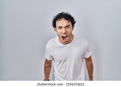 Hispanic man standing over isolated background angry and mad screaming frustrated and furious, shouting with anger. rage and aggressive concept. 