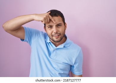 Hispanic man standing over pink background pointing unhappy to pimple on forehead, ugly infection of blackhead. acne and skin problem 