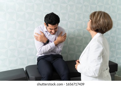 Hispanic Man Suffering From Fever Visiting Senior Female Doctor For Checkup In Clinic