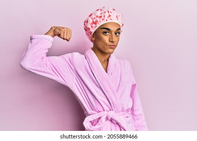 Hispanic Man Wearing Make Up Wearing Shower Towel Cap And Bathrobe Strong Person Showing Arm Muscle, Confident And Proud Of Power 