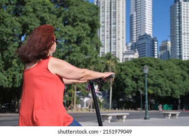 Hispanic mature woman riding her electric kick scooter around the city in summer. Concepts of sustainability, summer tourism, active life, clean energy and green mobility, eco transportation.