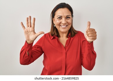 Hispanic Mature Woman Standing Over White Background Showing And Pointing Up With Fingers Number Six While Smiling Confident And Happy. 