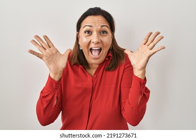 Hispanic Mature Woman Standing Over White Background Celebrating Crazy And Amazed For Success With Arms Raised And Open Eyes Screaming Excited. Winner Concept 