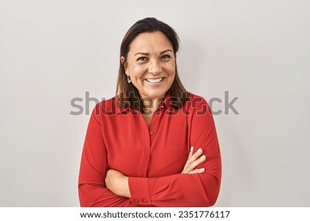 Hispanic mature woman standing over white background happy face smiling with crossed arms looking at the camera. positive person. 