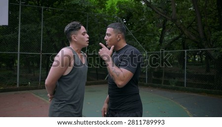 Hispanic men in heated argument on outdoor basketball court, pointing fingers and shouting as emotions escalate, camera circling around tense confrontation during street game