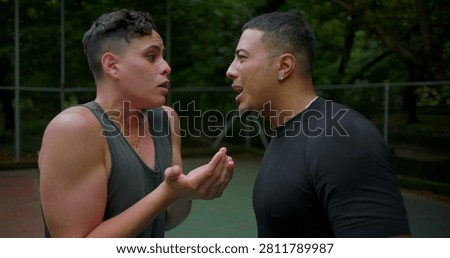 Hispanic men shouting and arguing on outdoor basketball court, faces close as emotions rise in intense street game confrontation and heated disagreement