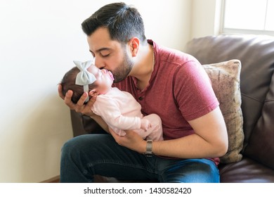 Hispanic Mid Adult Man Kissing Newborn Baby While Sitting On Sofa