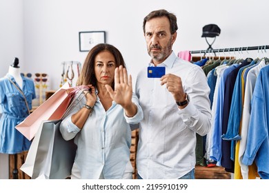 Hispanic Middle Age Couple Holding Shopping Bags And Credit Card Doing Stop Sing With Palm Of The Hand. Warning Expression With Negative And Serious Gesture On The Face. 