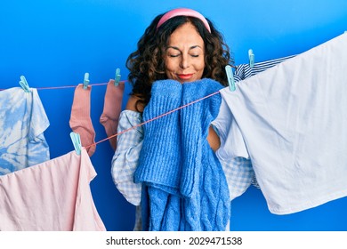 Hispanic Middle Age Woman Doing Laundry Smelling Scent From Clean Clothes