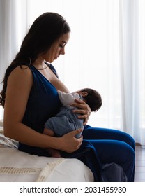 Hispanic mom breastfeeding her baby sitting on bed