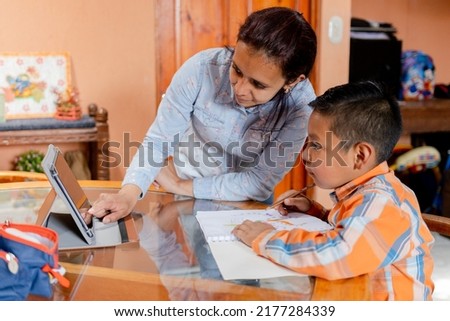 Hispanic mom helping her little son do her homework -homeschooling-young latin mother and her son learn online with tablet at home.